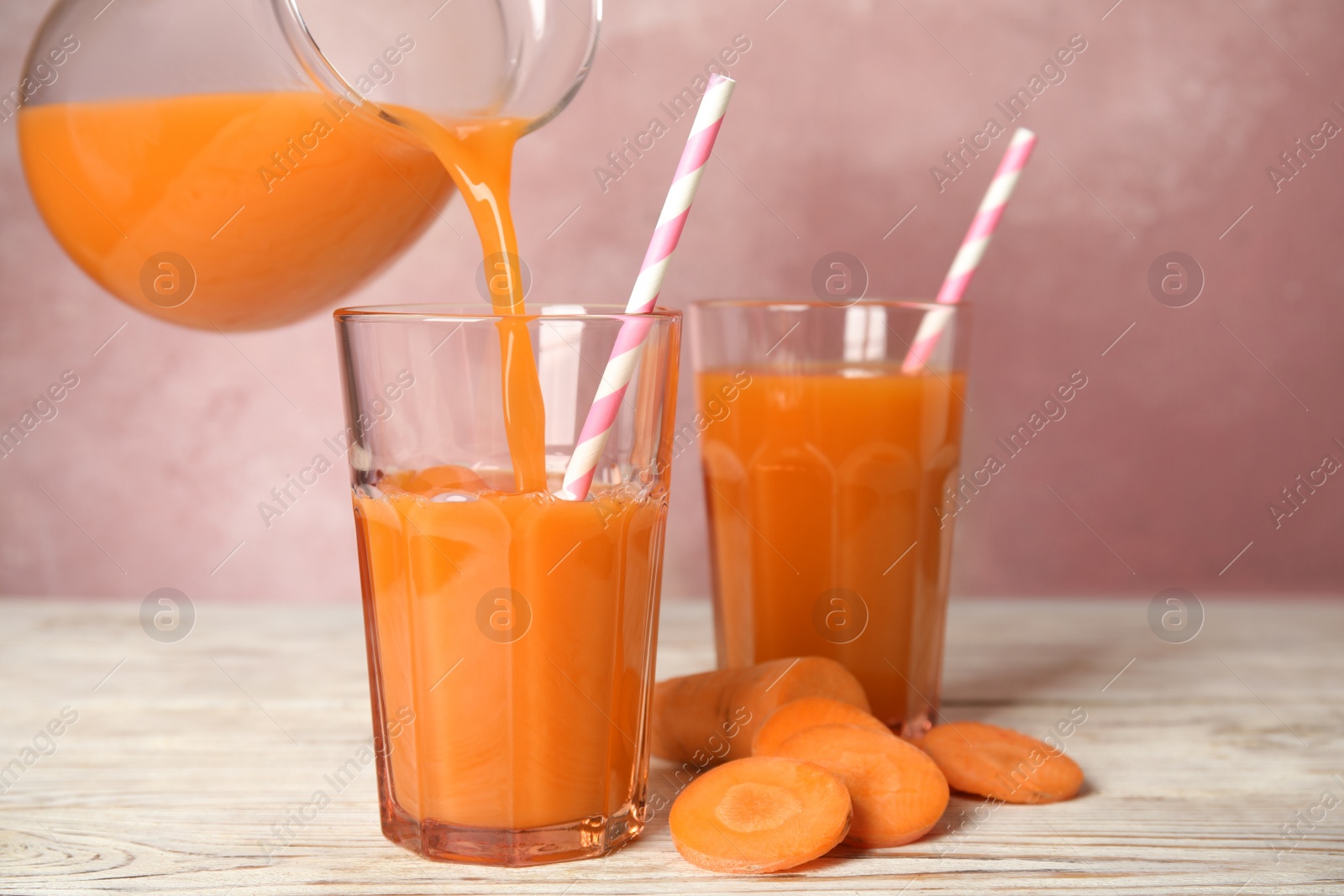 Photo of Pouring freshly made carrot juice into glass on wooden table