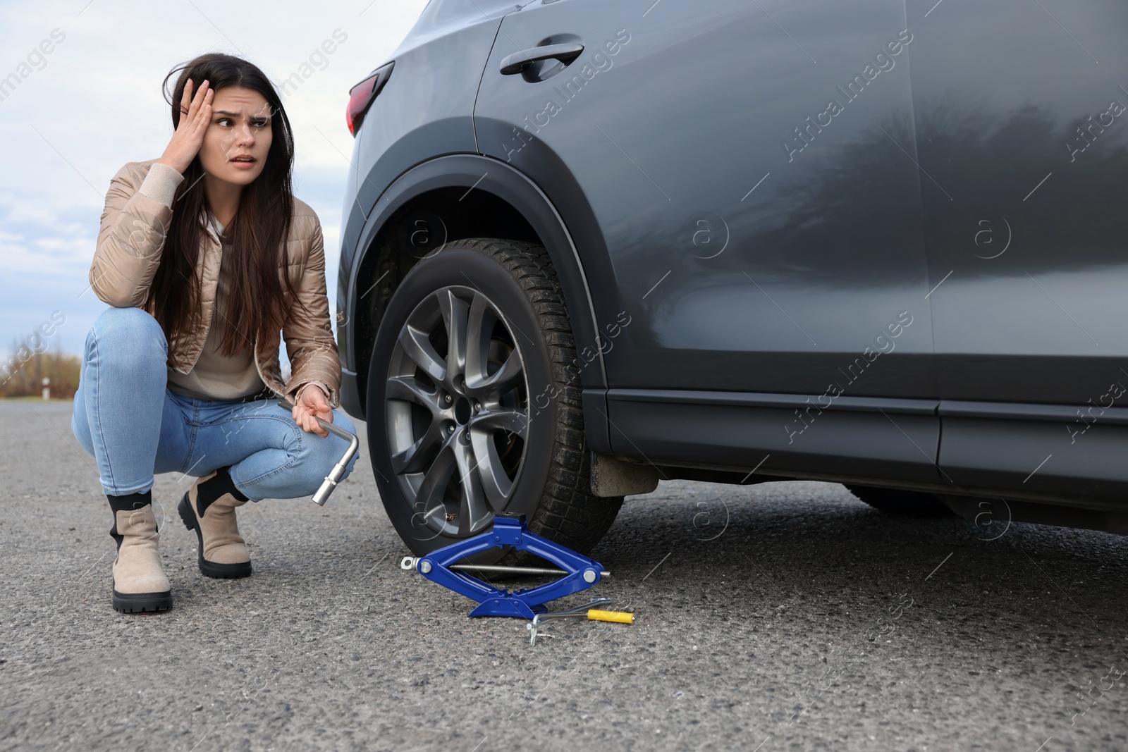 Photo of Worried young woman near car with punctured wheel on roadside