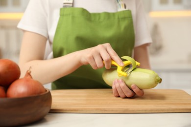 Photo of Woman peeling zucchini at table in kitchen, closeup. Preparing vegetable