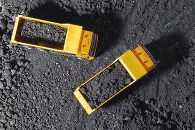 Toy tipper trucks with coal in field, flat lay