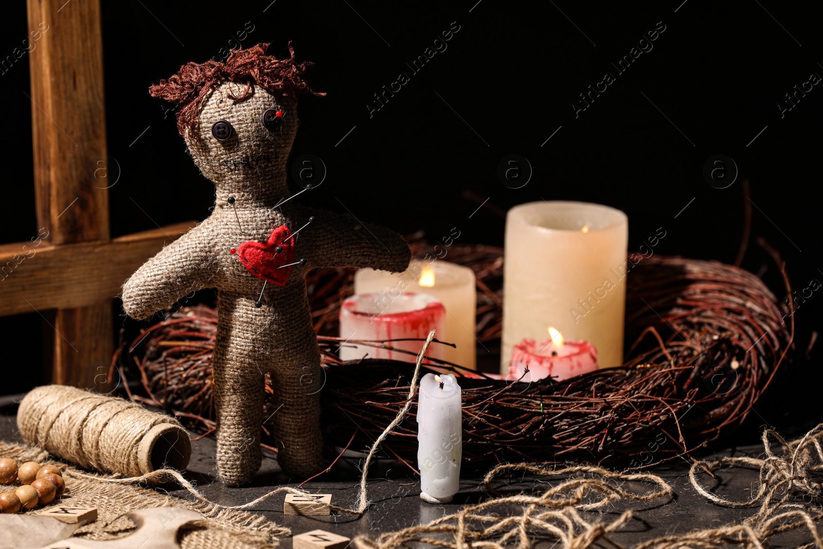 Photo of Voodoo doll with pins in heart and ceremonial items on black table