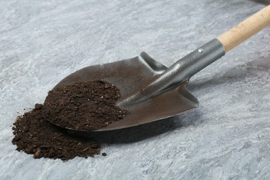 Photo of Metal shovel with fertile soil on gray textured surface