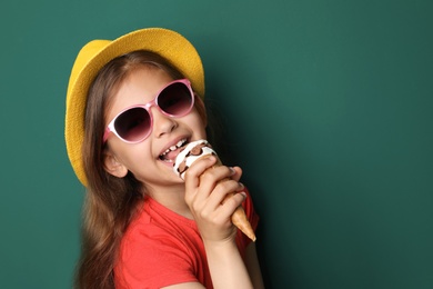 Cute little girl with delicious ice cream against color background, space for text