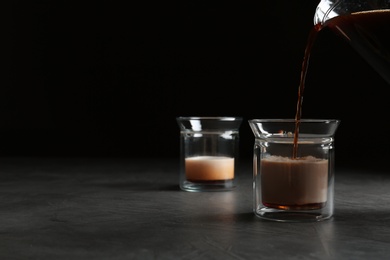 Photo of Pouring fresh coffee into glass on grey table. Space for text