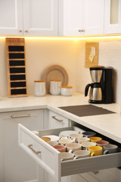 Photo of Open drawer with cups and coffeemaker on countertop in kitchen