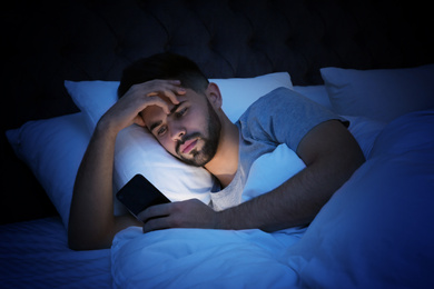 Young man addicted to smartphone in bed at night