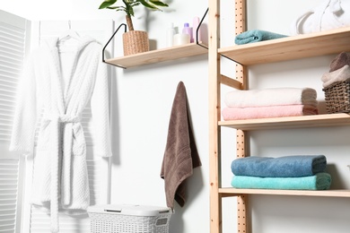 Photo of Clean towels and robe near white wall in modern bathroom interior