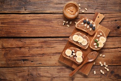 Photo of Toasts with tasty nut butter, banana slices, blueberries and peanuts on wooden table, flat lay. Space for text