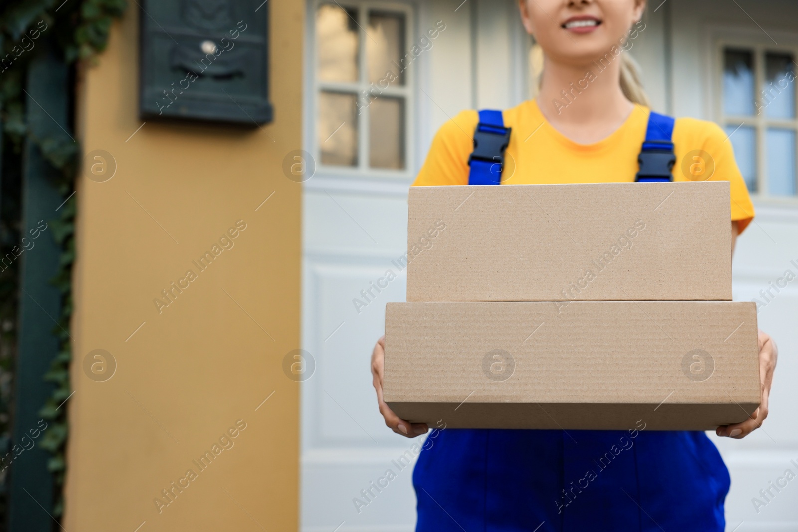 Photo of Courier in uniform with parcels near private house outdoors, closeup. Space for text