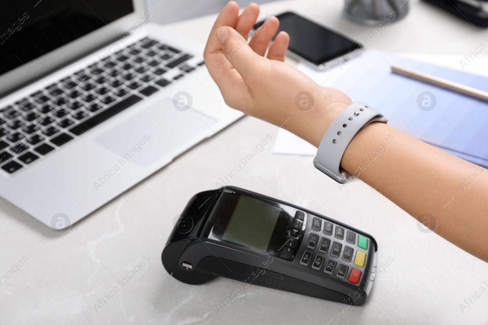 Photo of Woman using terminal for contactless payment with smart watch at table