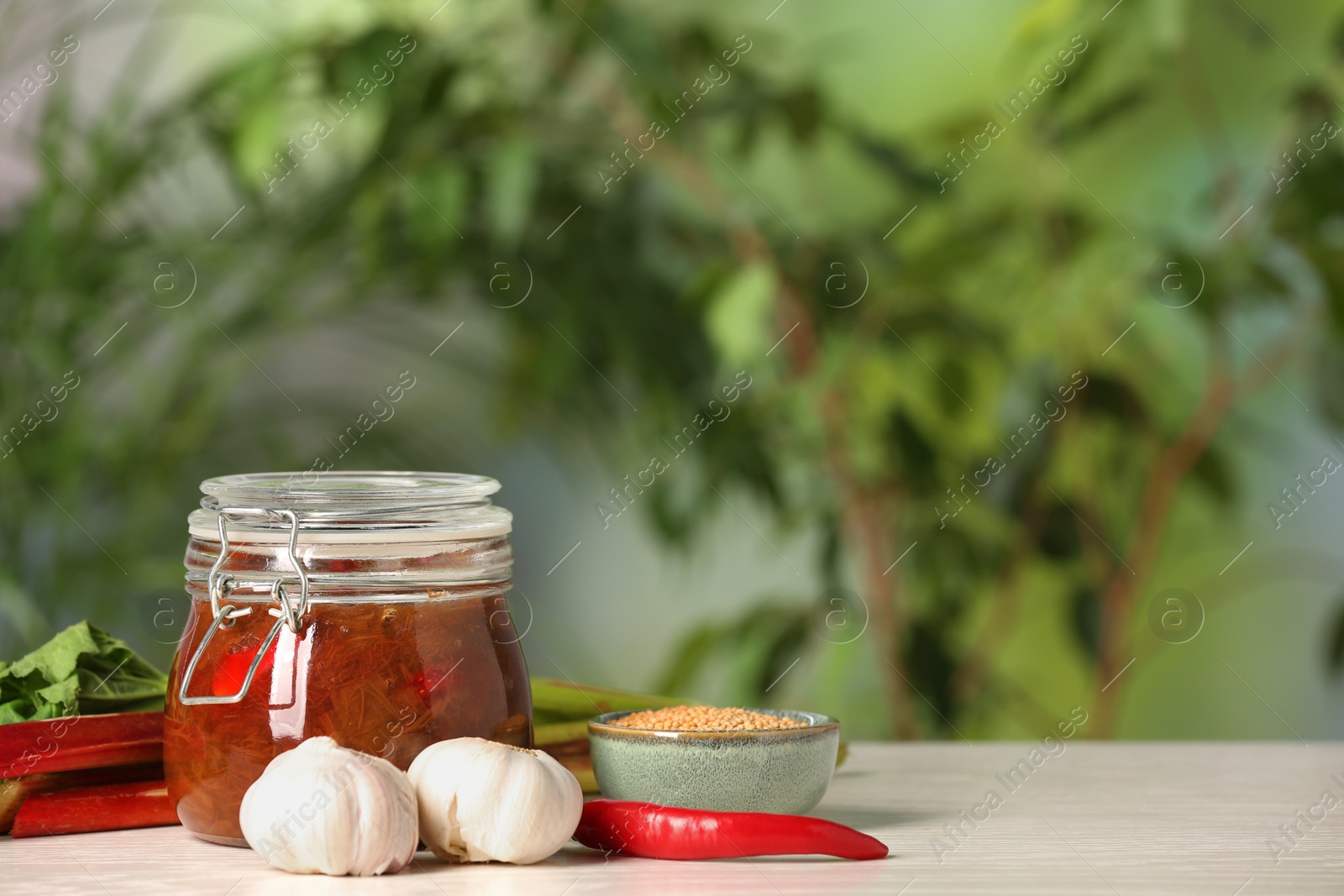 Photo of Tasty rhubarb sauce and ingredients on white table against blurred background , space for text