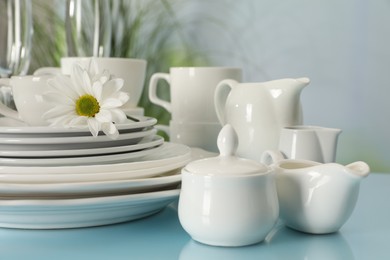 Set of clean dishware and flower on light blue table, closeup