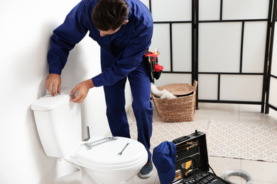 Professional plumber working with toilet bowl in bathroom