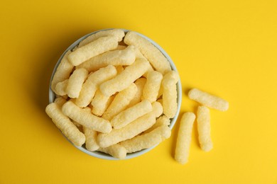 Photo of Bowl of corn sticks on yellow background, top view