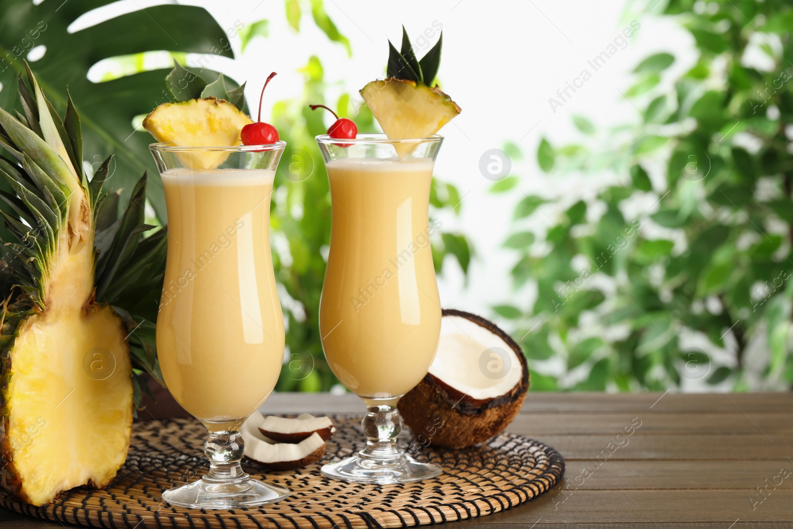 Photo of Tasty Pina Colada cocktails and ingredients on wooden table, space for text