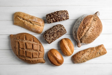 Photo of Different kinds of fresh bread on wooden table, flat lay.