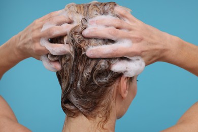 Woman washing hair on light blue background, closeup