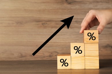 Image of Mortgage rate rising illustrated by upward arrow. Woman putting cube with percent sign on other ones at wooden table, closeup