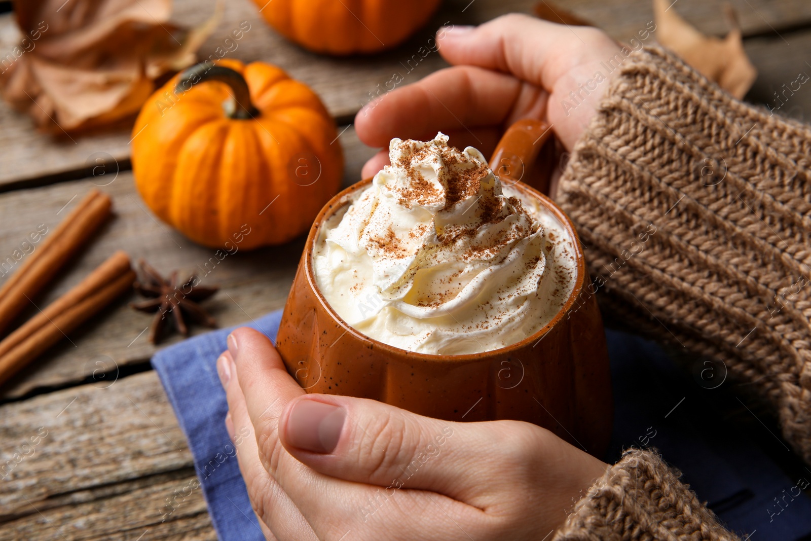 Photo of Woman holding mug of pumpkin spice latte with whipped cream at wooden table, closeup