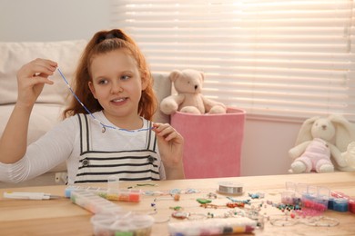 Photo of Cute girl with beautiful beaded jewelry at table in room