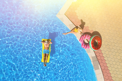 Young man with inflatable mattress in swimming pool near woman, top view. Summer vacation