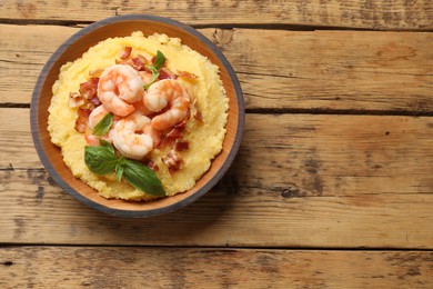 Photo of Fresh tasty shrimps, bacon, grits and basil in bowl on wooden table, top view. Space for text