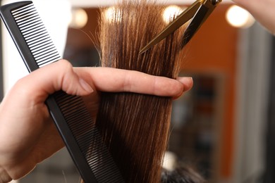 Hairdresser cutting client's hair with scissors in salon, closeup