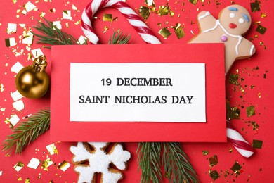 Photo of Card with text 19 December Saint Nicholas Day and festive decor on red background, flat lay