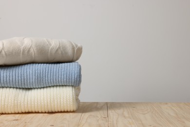 Photo of Stack of casual sweaters on wooden table against light background. Space for text
