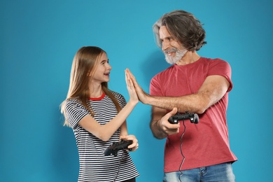 Mature man and teenage girl playing video games with controllers on color background