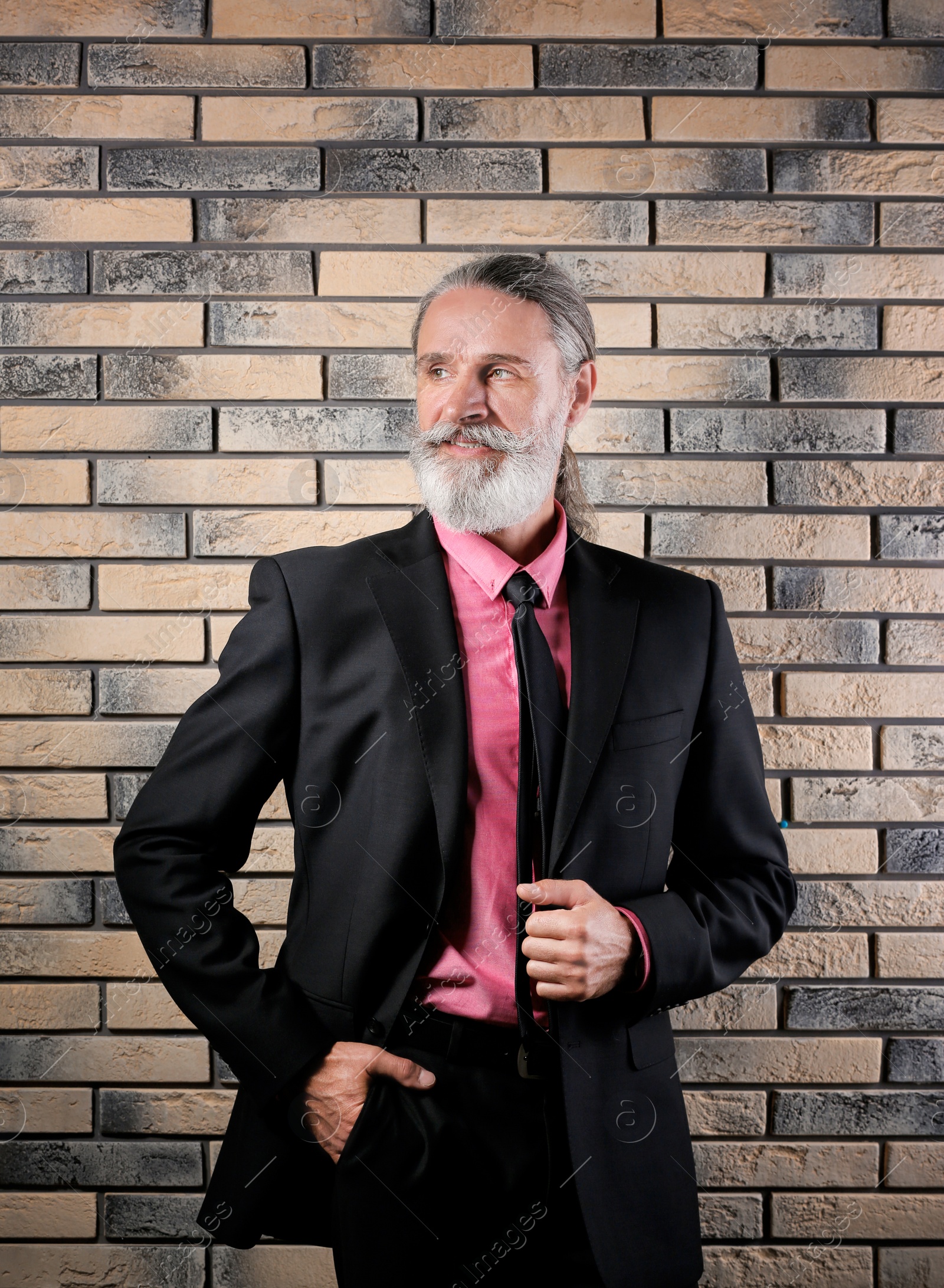 Photo of Handsome bearded mature man in suit near brick wall background