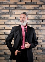 Photo of Handsome bearded mature man in suit near brick wall background