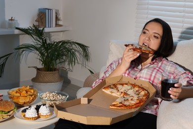 Photo of Overweight woman eating pizza with cola on sofa at home