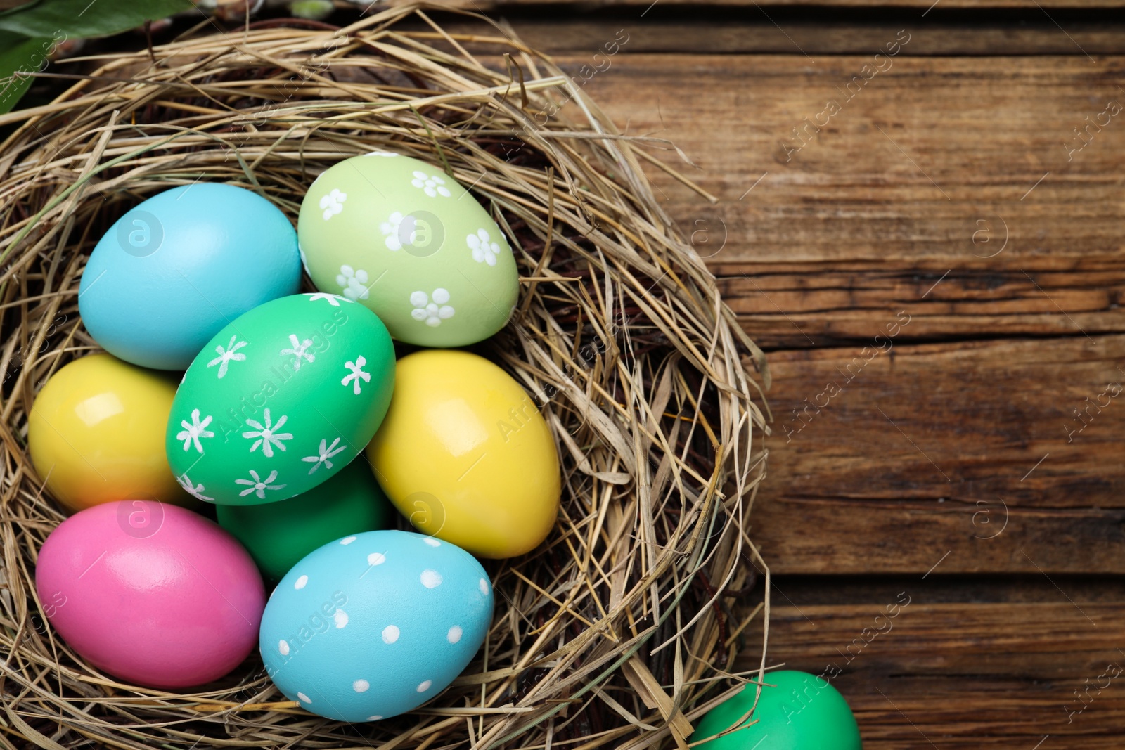 Photo of Colorful eggs in nest on wooden background. Happy Easter