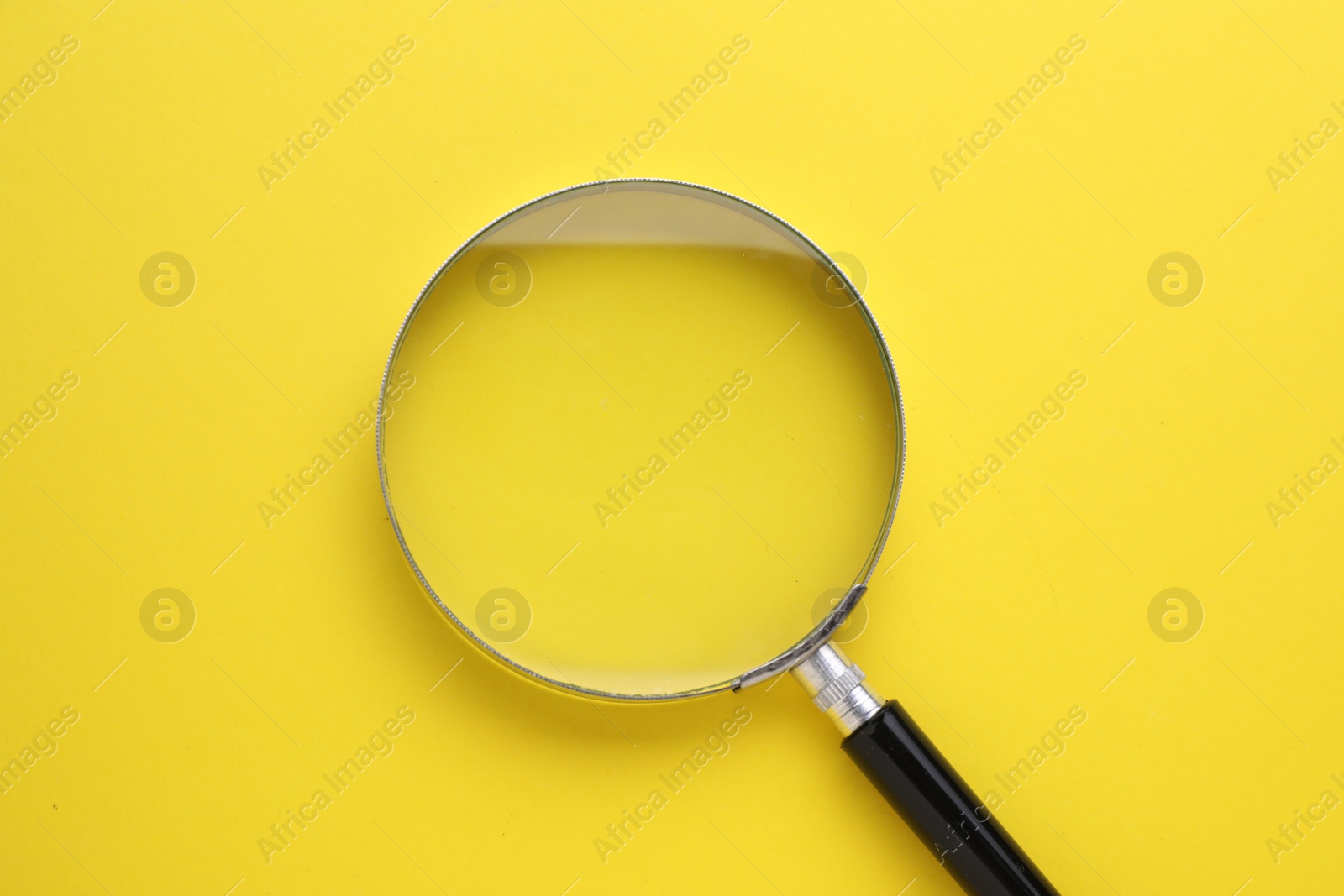 Photo of Magnifying glass on yellow background, top view