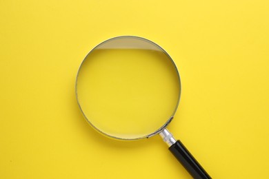 Magnifying glass on yellow background, top view