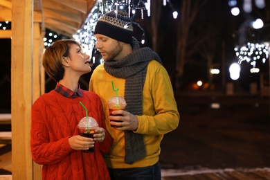 Photo of Young couple with cups of mulled wine at winter fair. Space for text