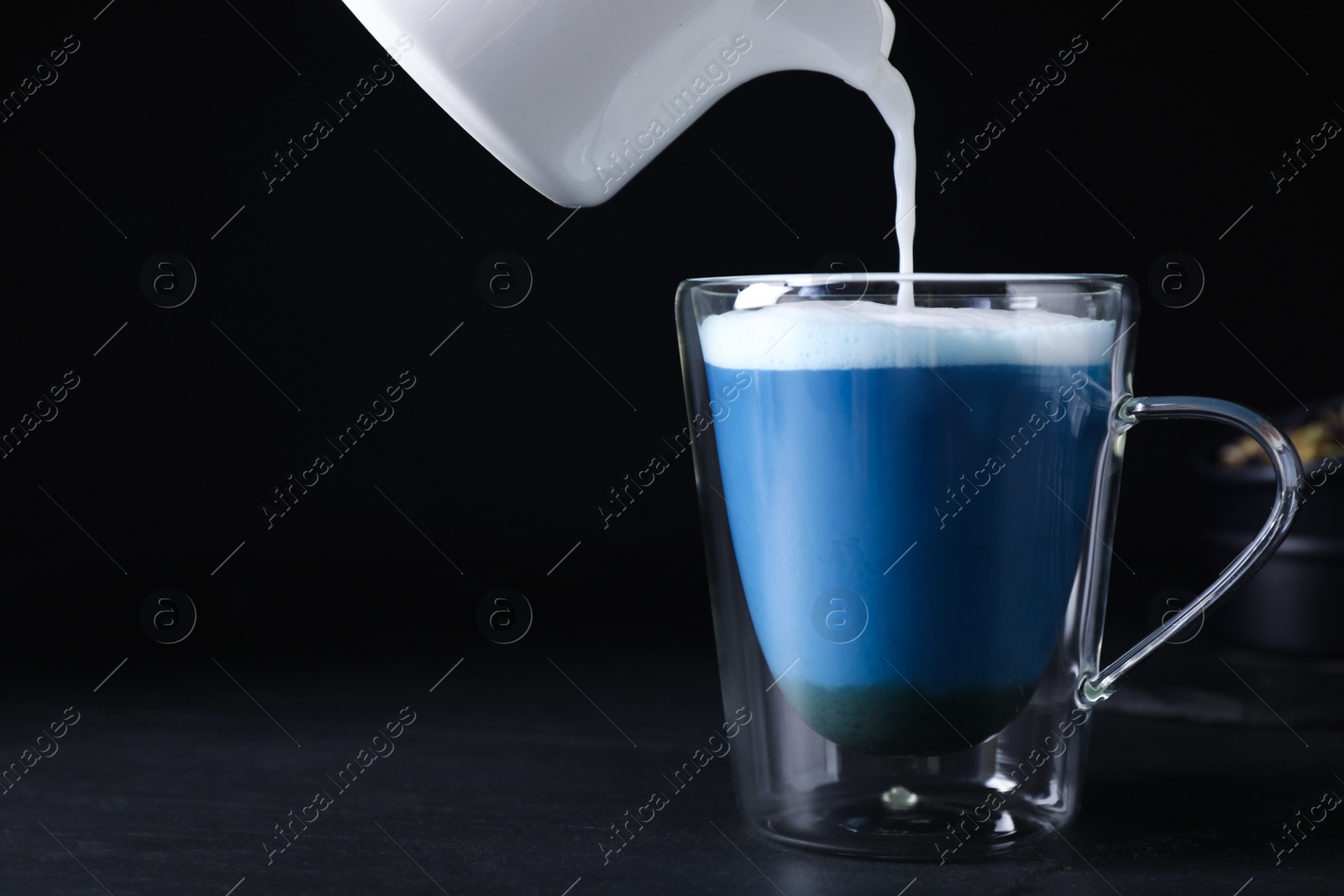 Photo of Pouring milk into glass cup with delicious blue matcha latte on black table. Space for text