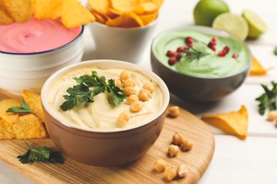 Bowl of delicious classic hummus with parsley on white wooden table. Space for text