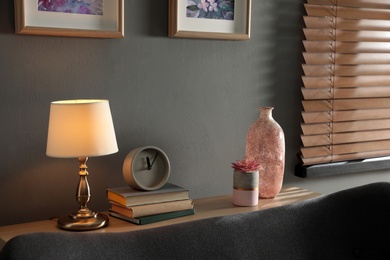Photo of Lamp, clock, books and decor elements on table in living room. Interior design