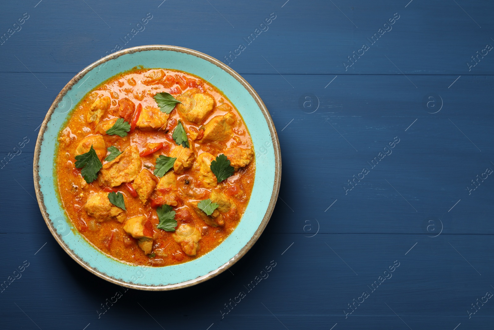 Photo of Delicious chicken curry on blue wooden table, top view. Space for text