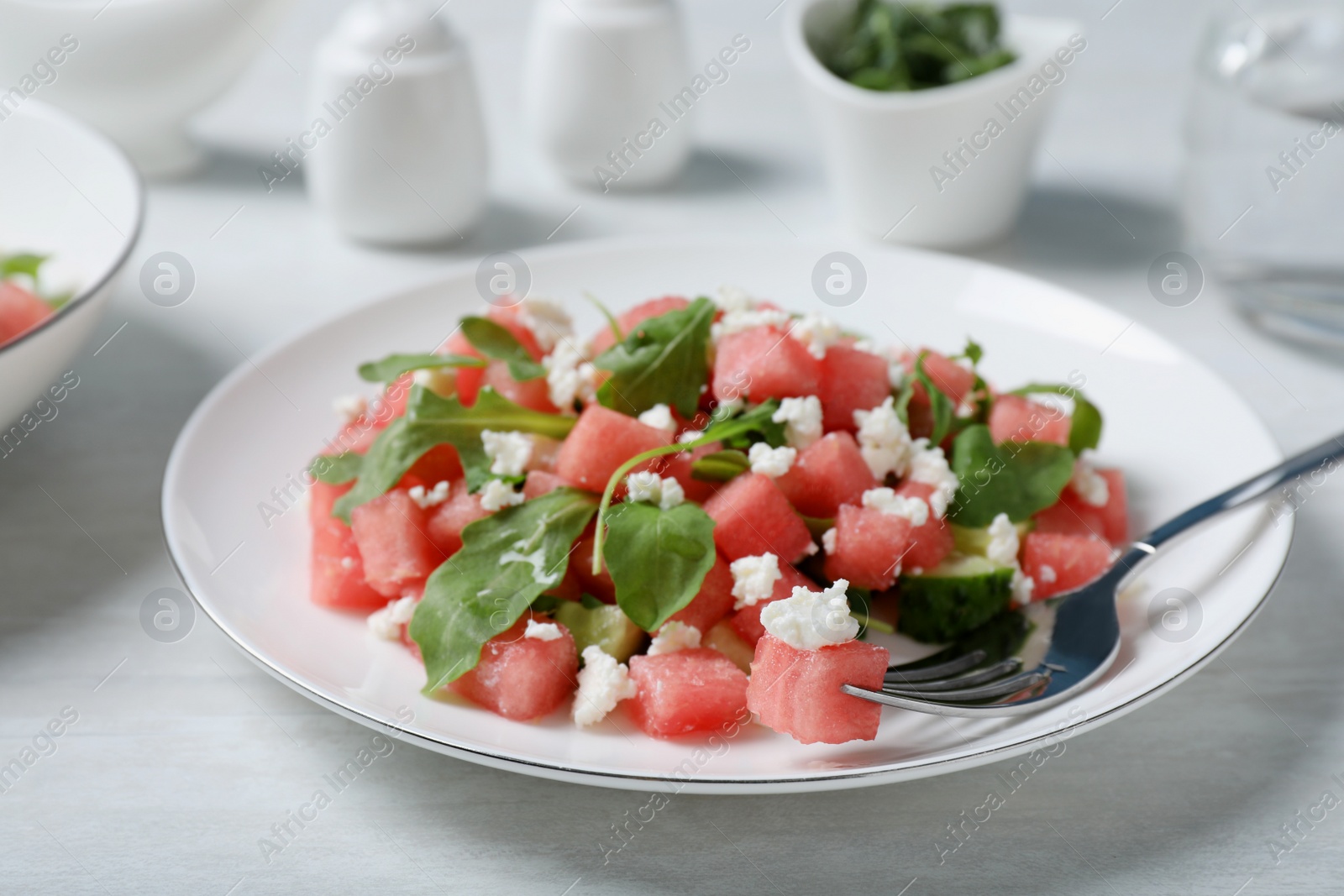 Photo of Delicious salad with watermelon, cucumber, arugula and feta cheese served on white wooden table, closeup