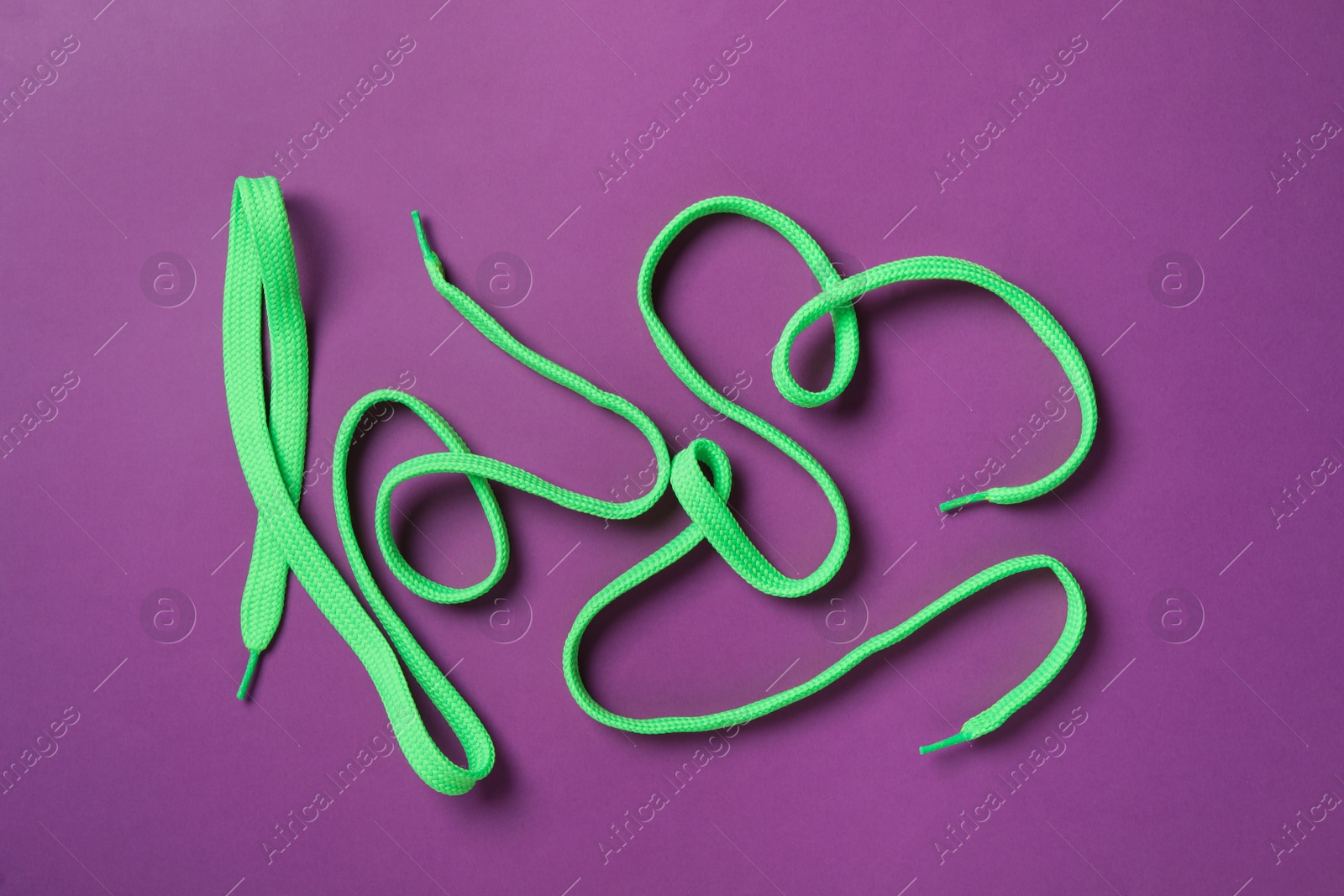 Photo of Green shoelaces on purple background, flat lay