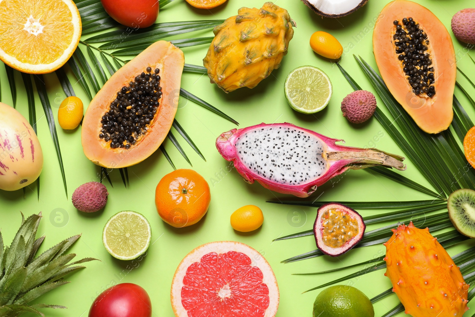 Photo of Different exotic fruits and palm leaves on green background, flat lay