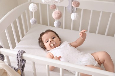Cute little baby lying in crib with hanging mobile