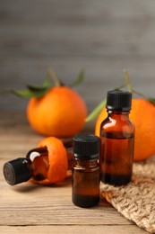 Photo of Bottles of tangerine essential oil, fresh fruit and peel on wooden table