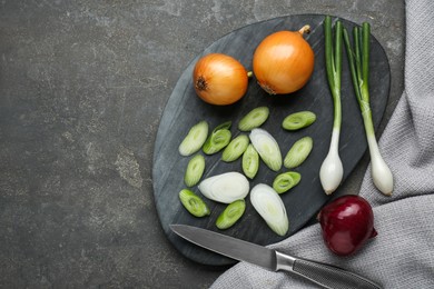 Board with different kinds of onions and knife on grey table, flat lay. Space for text