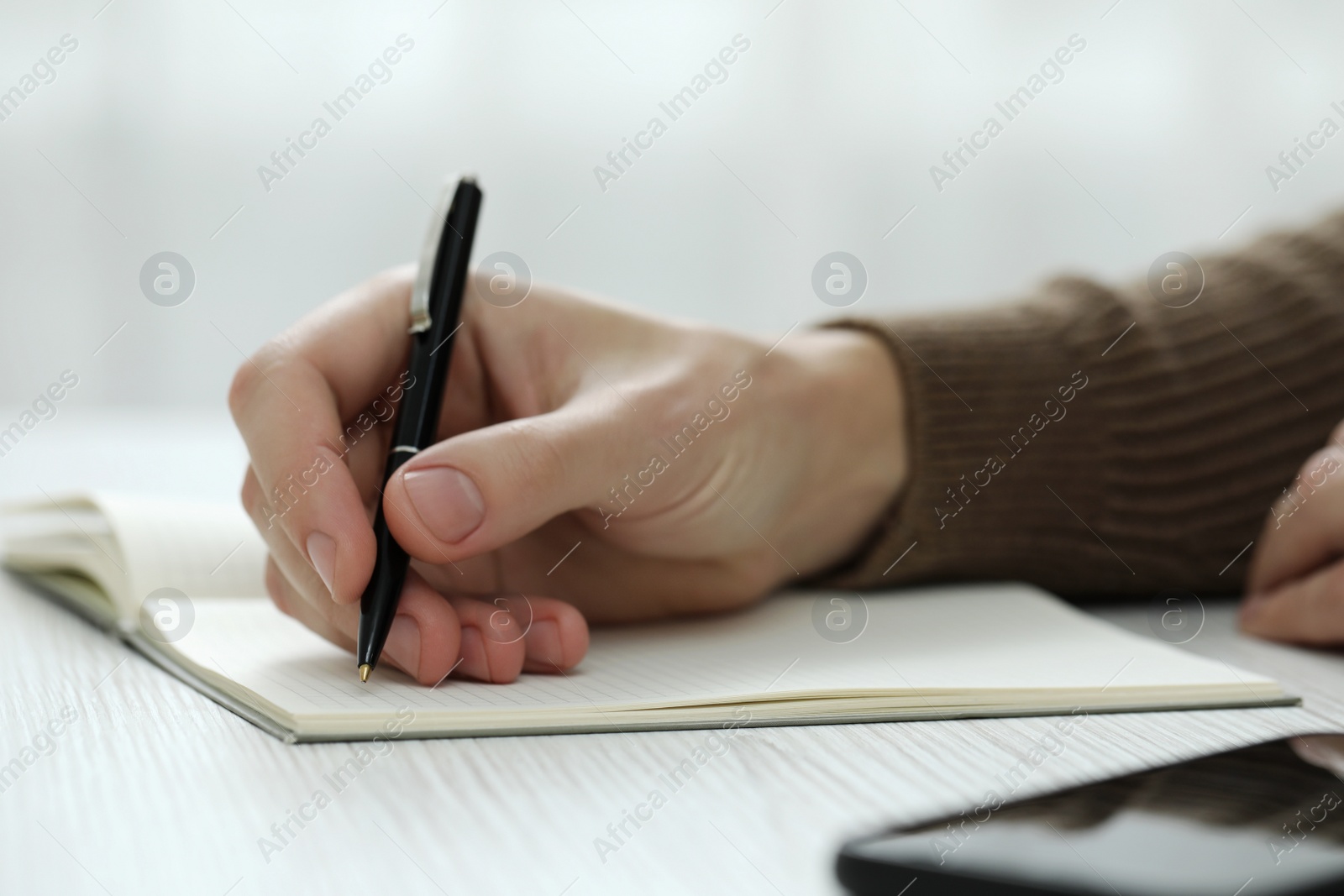 Photo of Man writing in notebook at white wooden table, closeup