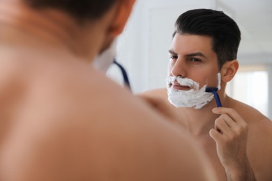 Photo of Handsome man shaving near mirror in bathroom