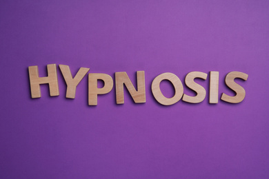 Photo of Word HYPNOSIS made with wooden letters on purple background, flat lay